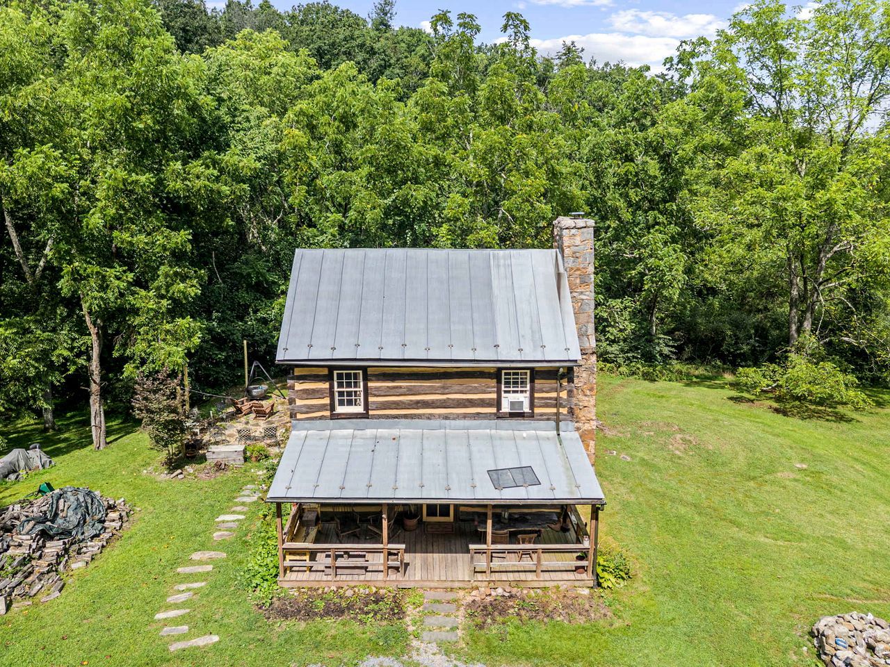 A log cabin with a metal roof, a front porch, and a stone chimney.
