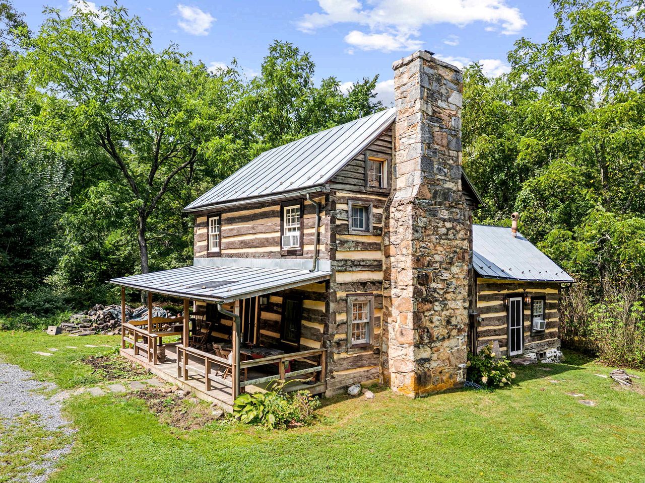 A log cabin with a stone chimney, a porch with seating, and a small attached structure.