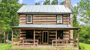 A log cabin with a porch, two windows, and a chimney.