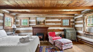 A log cabin bedroom with a bed, fireplace, chair, dresser, and two windows.