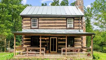 A log cabin with a porch, two windows, and a chimney.