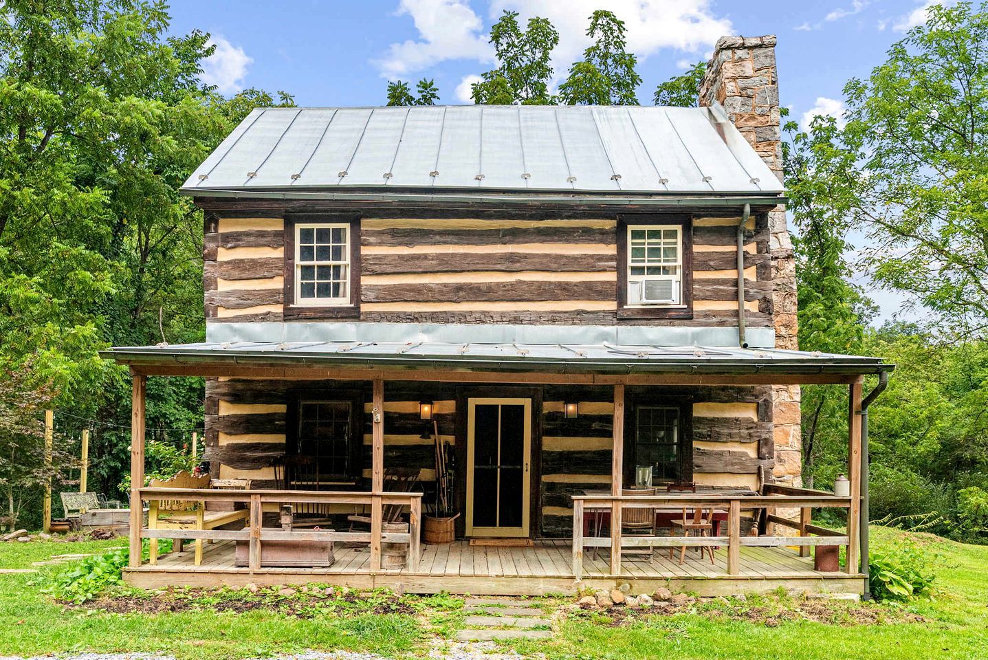 A log cabin with a porch, two windows, and a chimney.