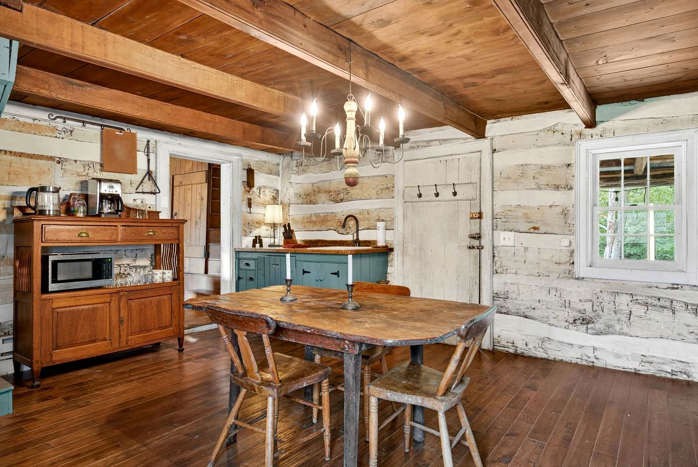 A rustic kitchen with wooden cabinets, a dining table, and a chandelier.