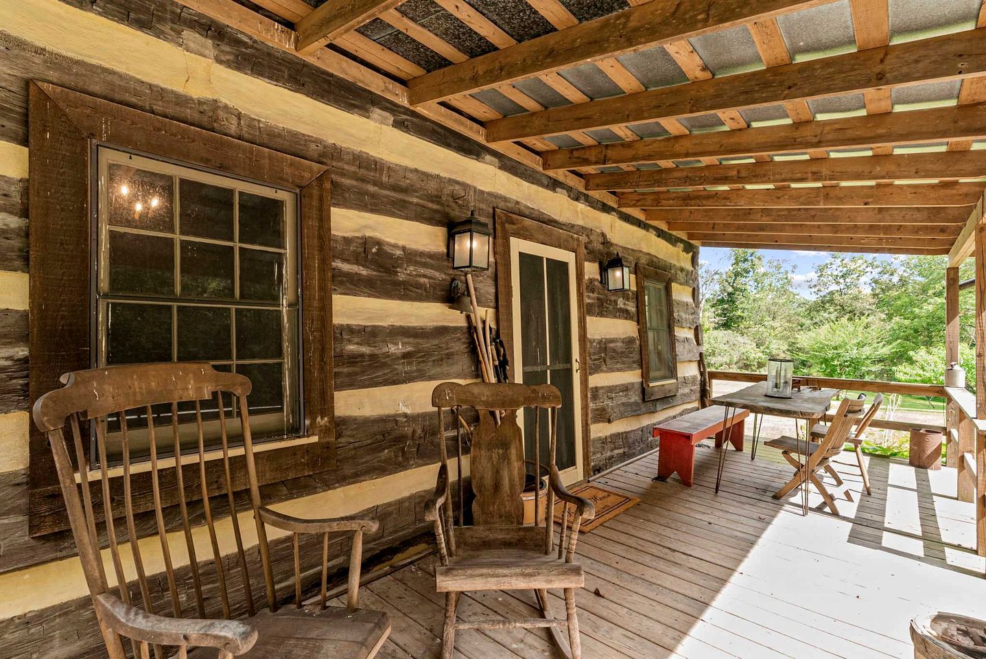 A rustic cabin with a wooden deck, a table with chairs, and a large window.