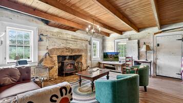 A rustic interior with a stone fireplace, wooden beams, a television, and a cozy seating area.