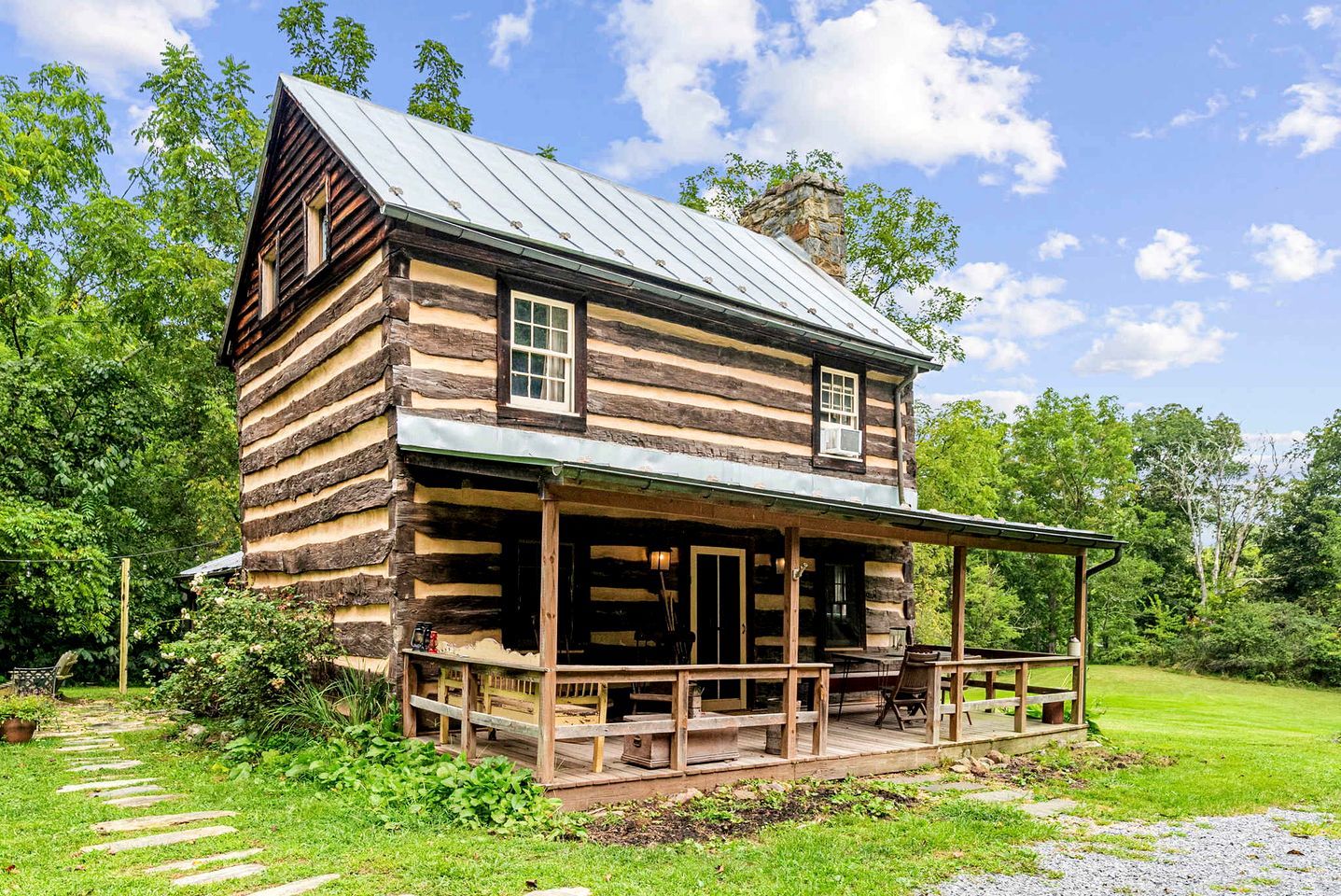 A log cabin with a porch, surrounded by greenery.