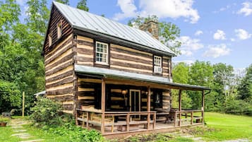 A log cabin with a porch, surrounded by greenery.