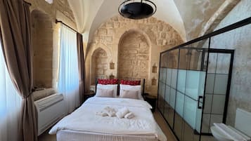 Un dormitorio con una cama grande, una lámpara colgante, paredes de piedra y cabina de ducha de vidrio.