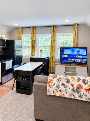 A compact living space with a kitchenette, a dining area, and a television displaying a movie. - Cute, Small, but Mighty! (Omaha)