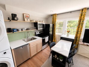 A compact kitchen with a dishwasher, microwave, stove, and refrigerator. There is a small dining area with a table and chairs. - Cute, Small, but Mighty! (Omaha)