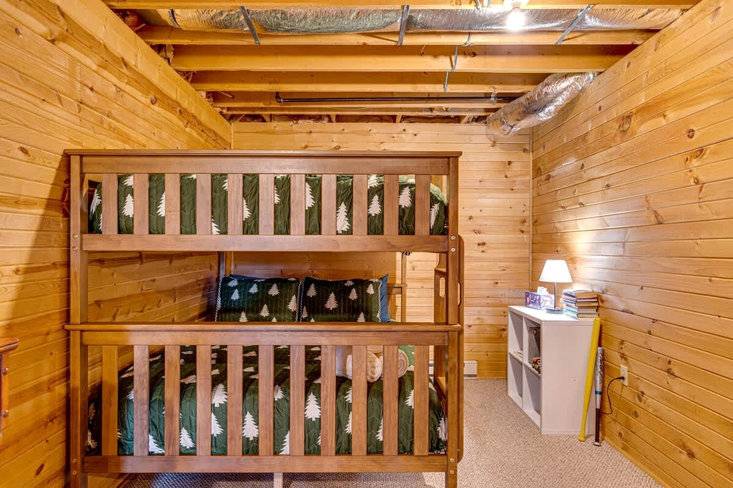A wooden room with bunk beds, a small table with a lamp, and a shelf with books.
