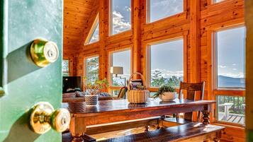 A wooden interior with a dining table, benches, and large windows offering a view of the outdoors.