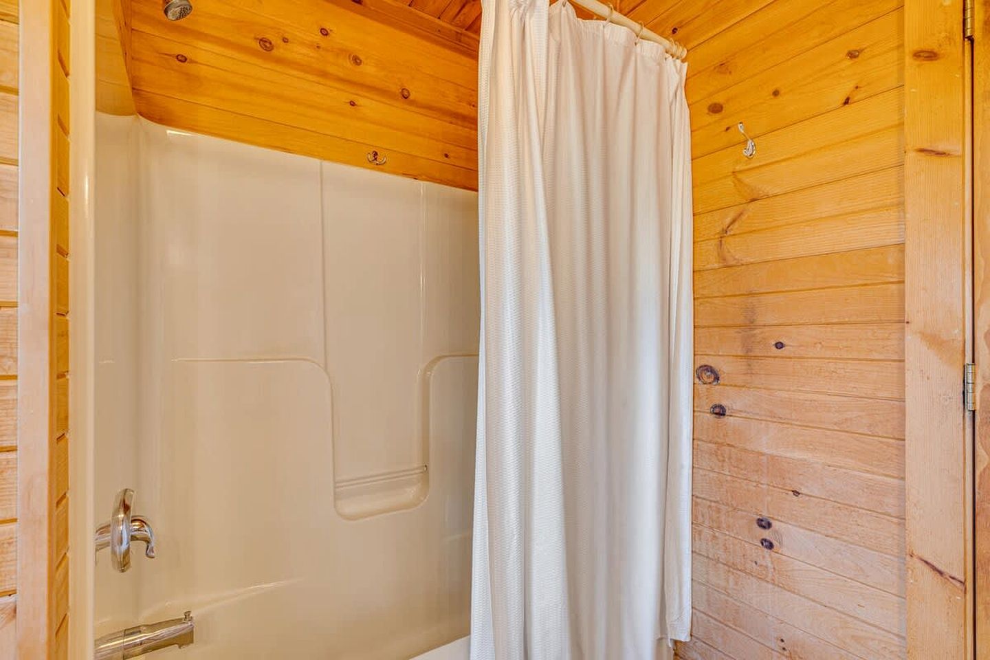 Una cabaña de madera con zona de ducha, una puerta con pomo y una cortina.