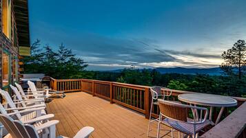 A wooden deck with outdoor seating, a table, and a view of the surrounding landscape.