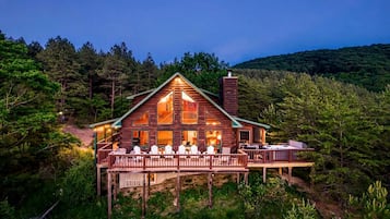 A log cabin with a deck, surrounded by forest.