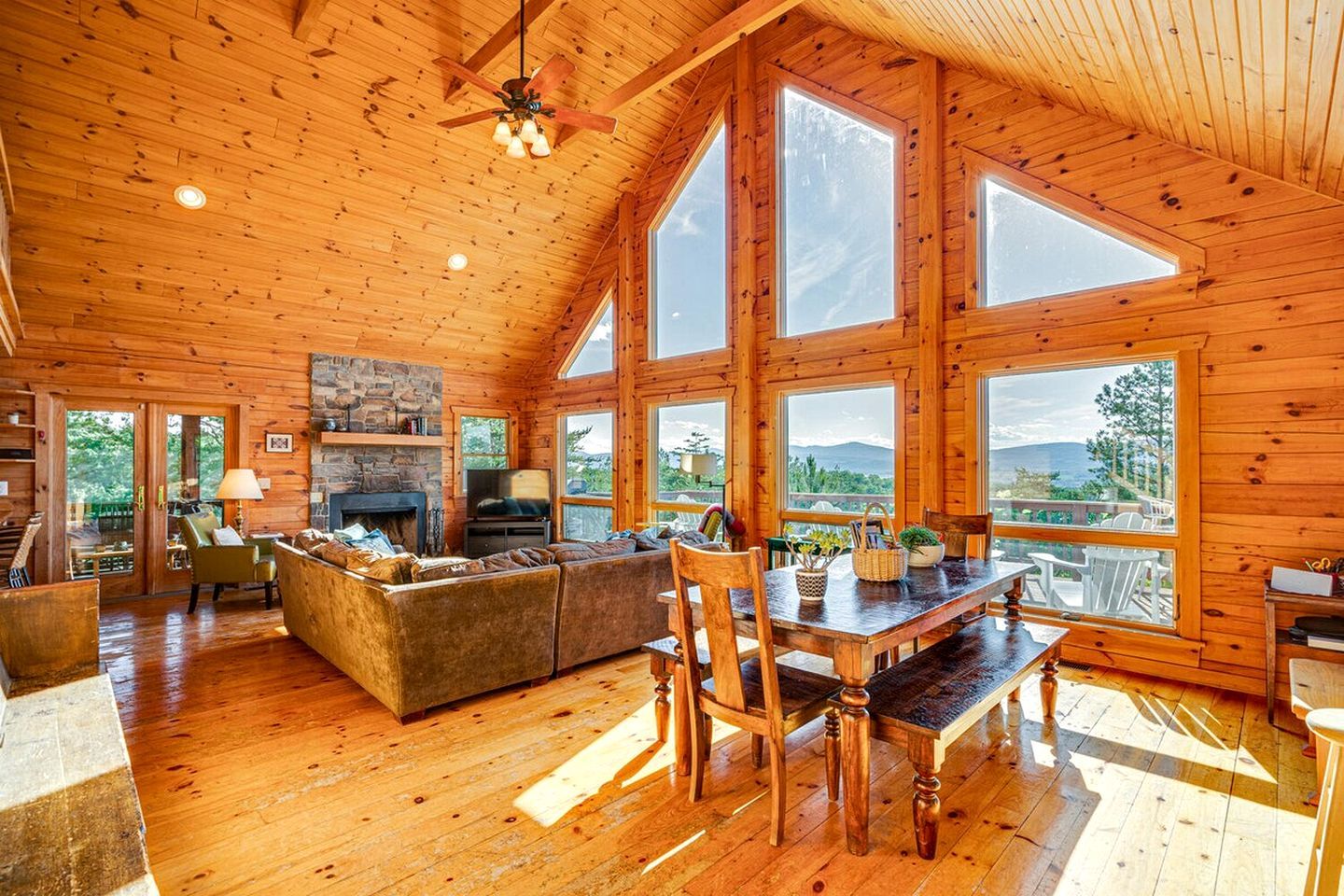A spacious cabin with a stone fireplace, wooden furniture, and large windows offering views of the outdoors.