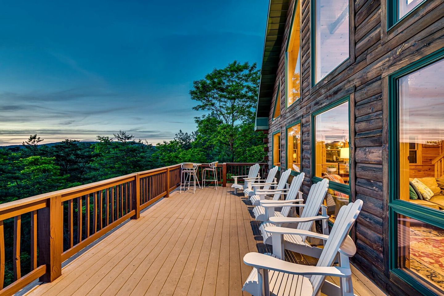 A wooden deck with white chairs and a table, overlooking a forested landscape.