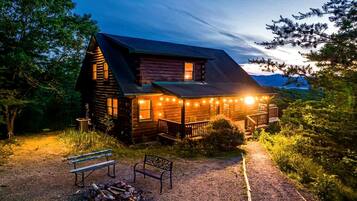 A log cabin with a porch, a fire pit, and a bench.