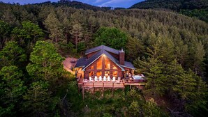 A log cabin with a deck and hot tub, surrounded by dense forest.
