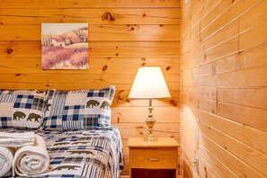 Quarto de cabana de madeira com cama, mesa de cabeceira, abajur e um quadro na parede.