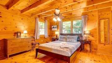 A wooden cabin bedroom with a bed, two nightstands, a dresser, and a ceiling fan.