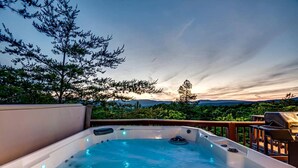 A hot tub on a deck with a view of trees and mountains.