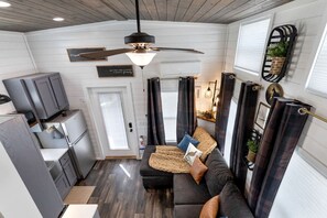 Ein kompakter Wohnbereich mit Küchenzeile, Deckenventilator, einer Couch mit Kissen und einem kleinen Esstisch.