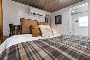 Een slaapkamer met een bed, kussens, een spiegel en een berenthema schilderij.