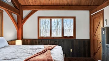 A bedroom with a large bed, wooden beams, a window with a view, and a door.
