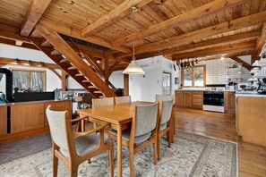 A spacious kitchen with wooden beams, a dining area with a table and chairs, and a staircase leading to another level. - Charming Post-and-Beam Mountain Cabin with Hot Tub Near Berkeley Springs | Great Cacapon, WV (Great Cacapon)