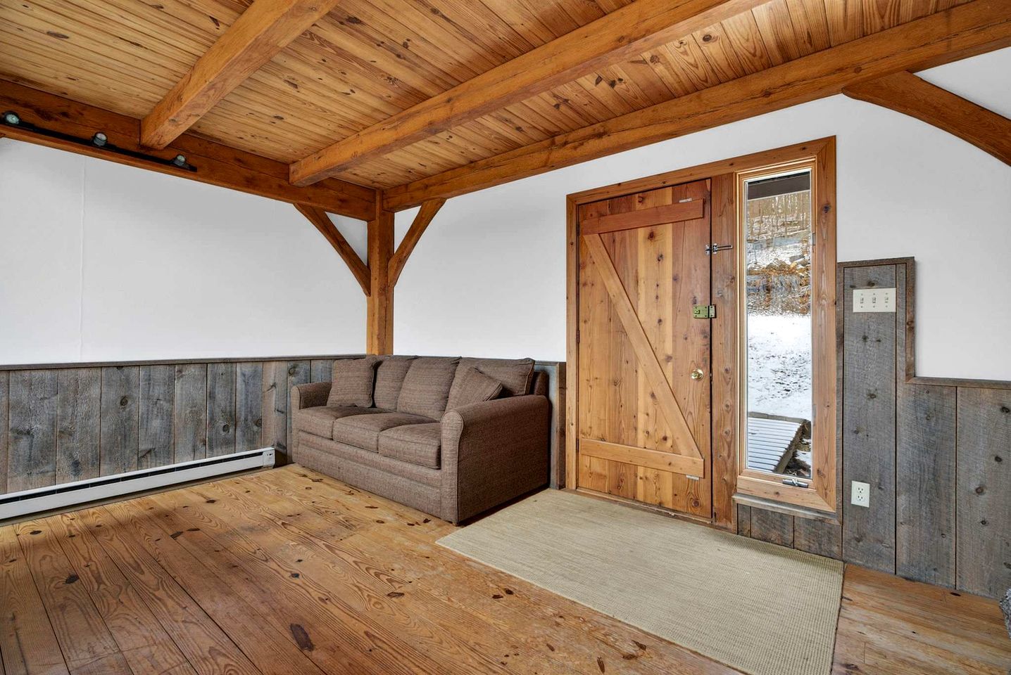 A wooden ceiling with exposed beams, a brown sofa, and a wooden door with a glass panel.