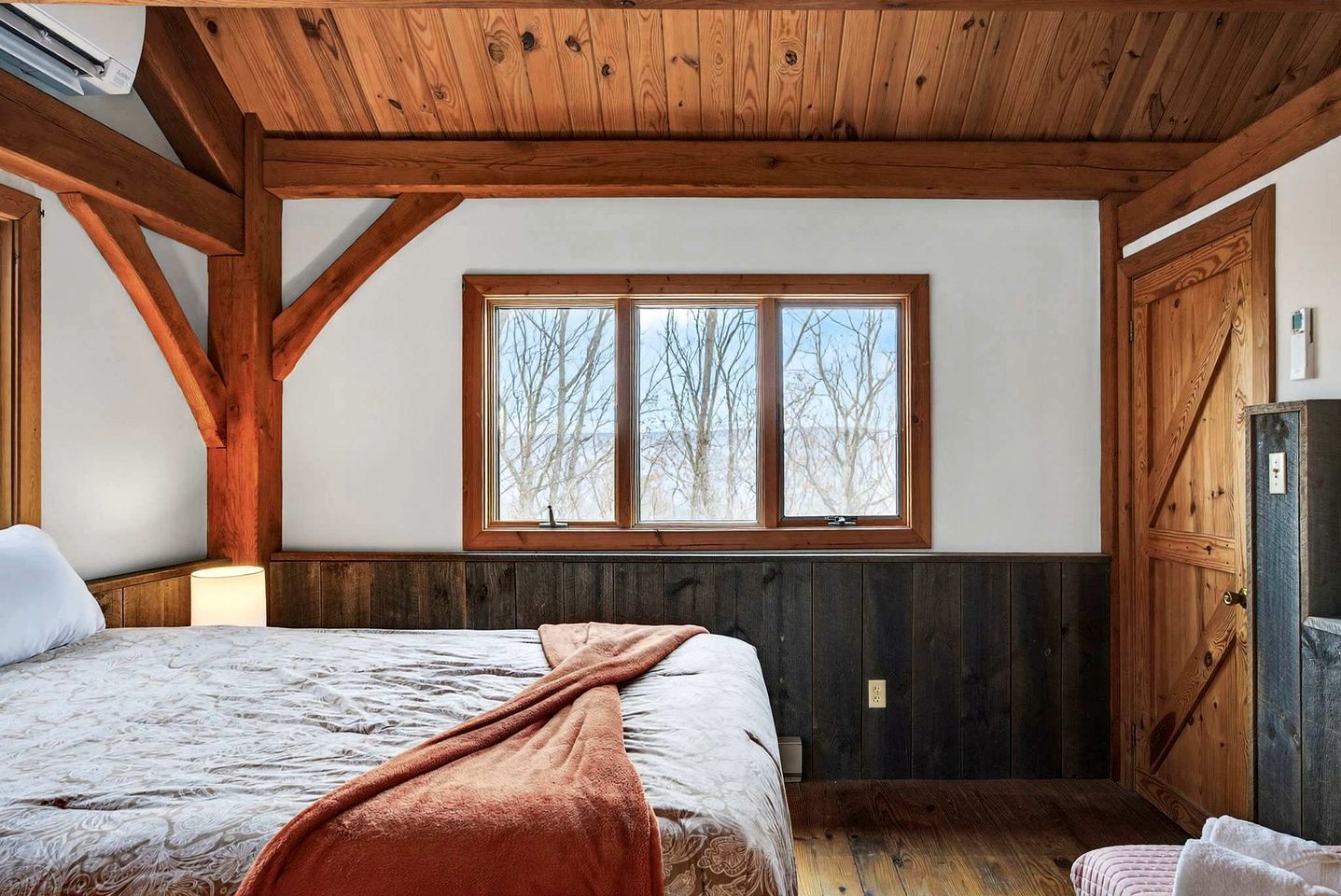 Un dormitorio con una cama grande, vigas de madera, una ventana con vistas y una puerta.