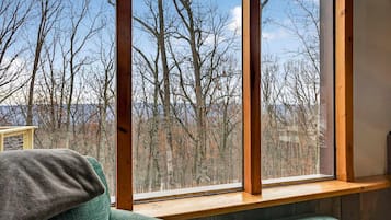 A room with a large window, a wooden bench, and a view of leafless trees.