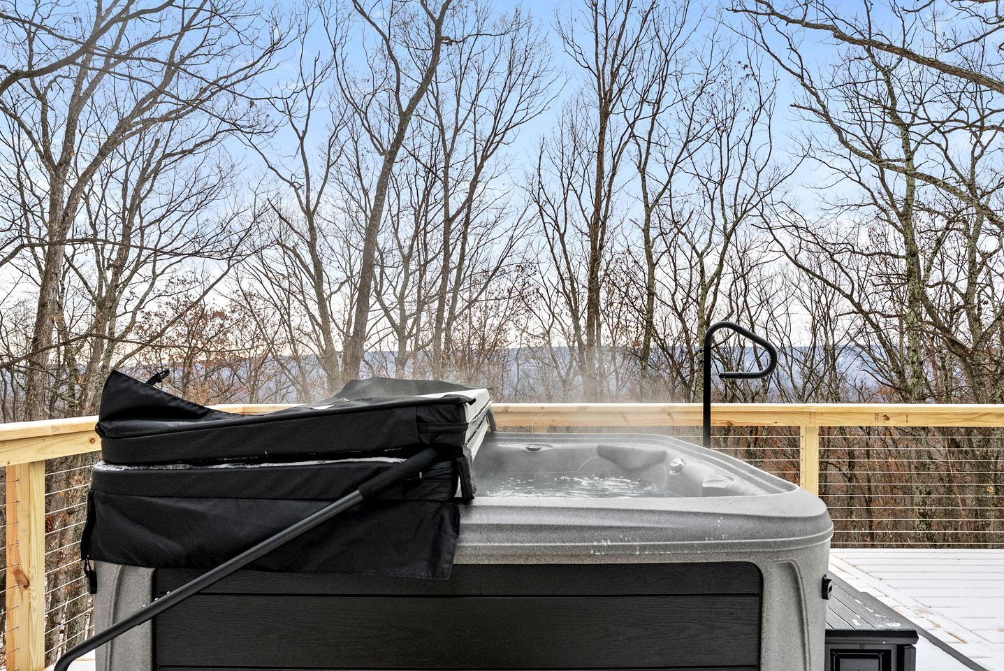 A hot tub on a wooden deck with a view of leafless trees and a clear sky.