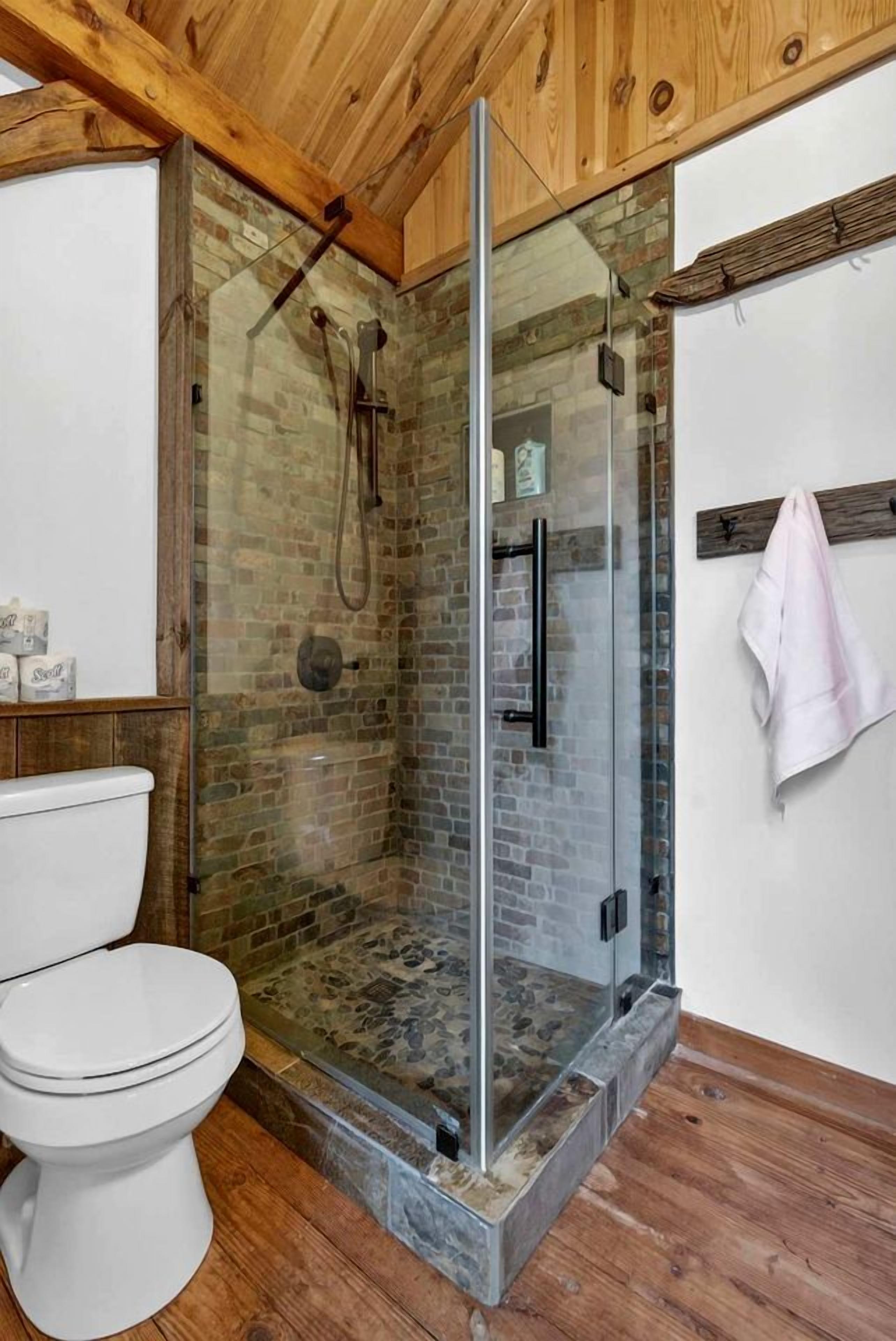 A bathroom with a glass-enclosed shower, a white toilet, and wooden flooring.