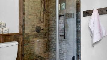 A bathroom with a glass-enclosed shower, a white toilet, and wooden flooring.