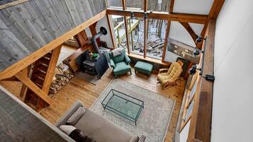 A spacious loft-style living area with a high ceiling, wooden beams, and a large window overlooking a snowy landscape.
