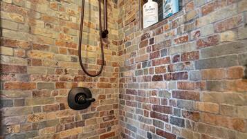 A shower with a brick wall, a handheld showerhead, and toiletries on a shelf.