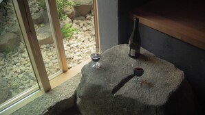 Une table en pierre, sur laquelle sont posés une bouteille de vin et deux verres à vin, est placée près d’une porte vitrée donnant sur un espace extérieur agrémenté de rochers et de verdure.