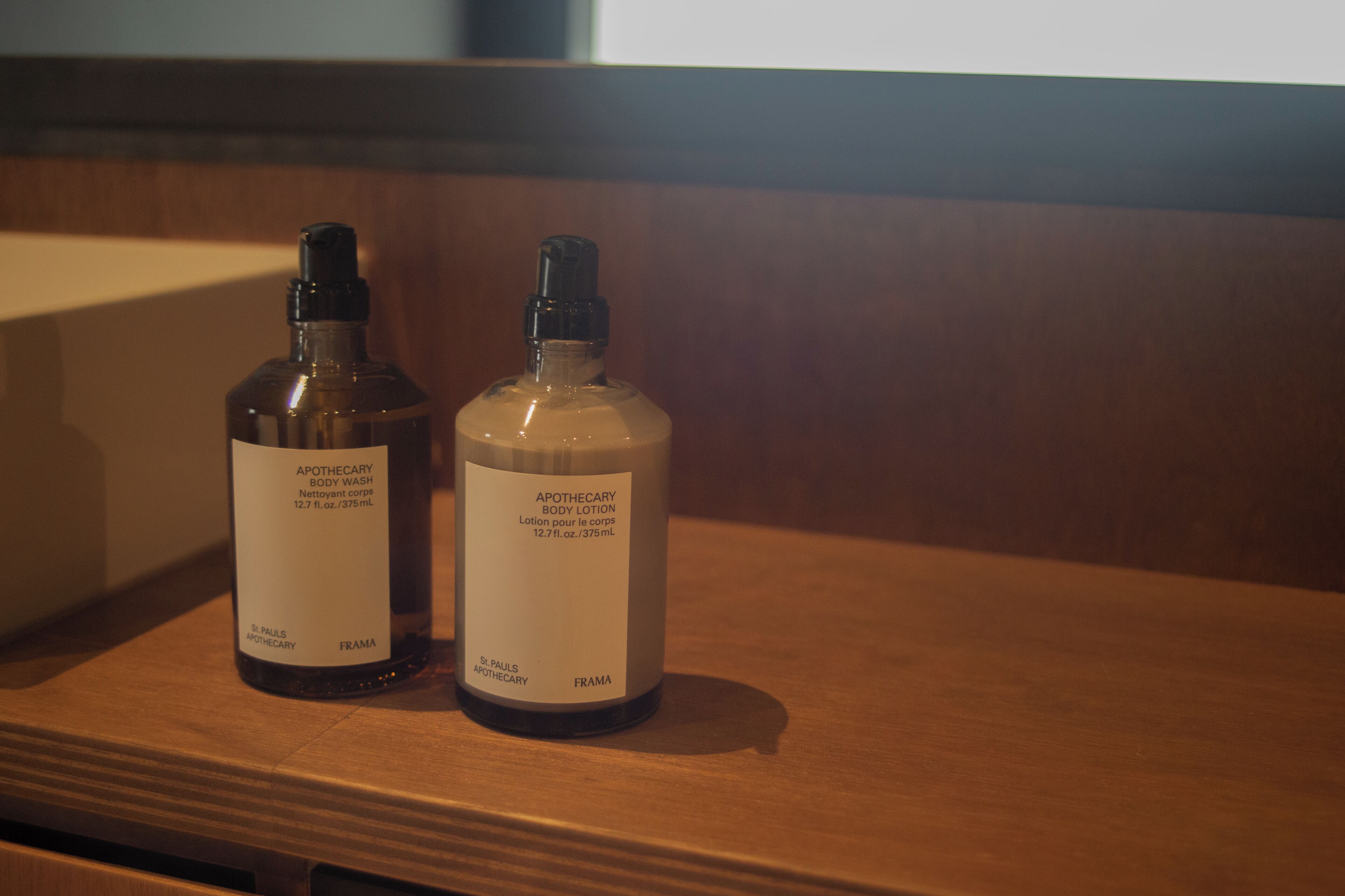 Two bottles of body wash and lotion on a wooden shelf.