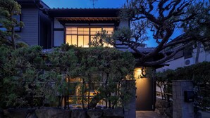 Une maison traditionnelle japonaise, dotée d’une entrée en pierre, entourée de pins et agrémentée d’un jardin bien entretenu.