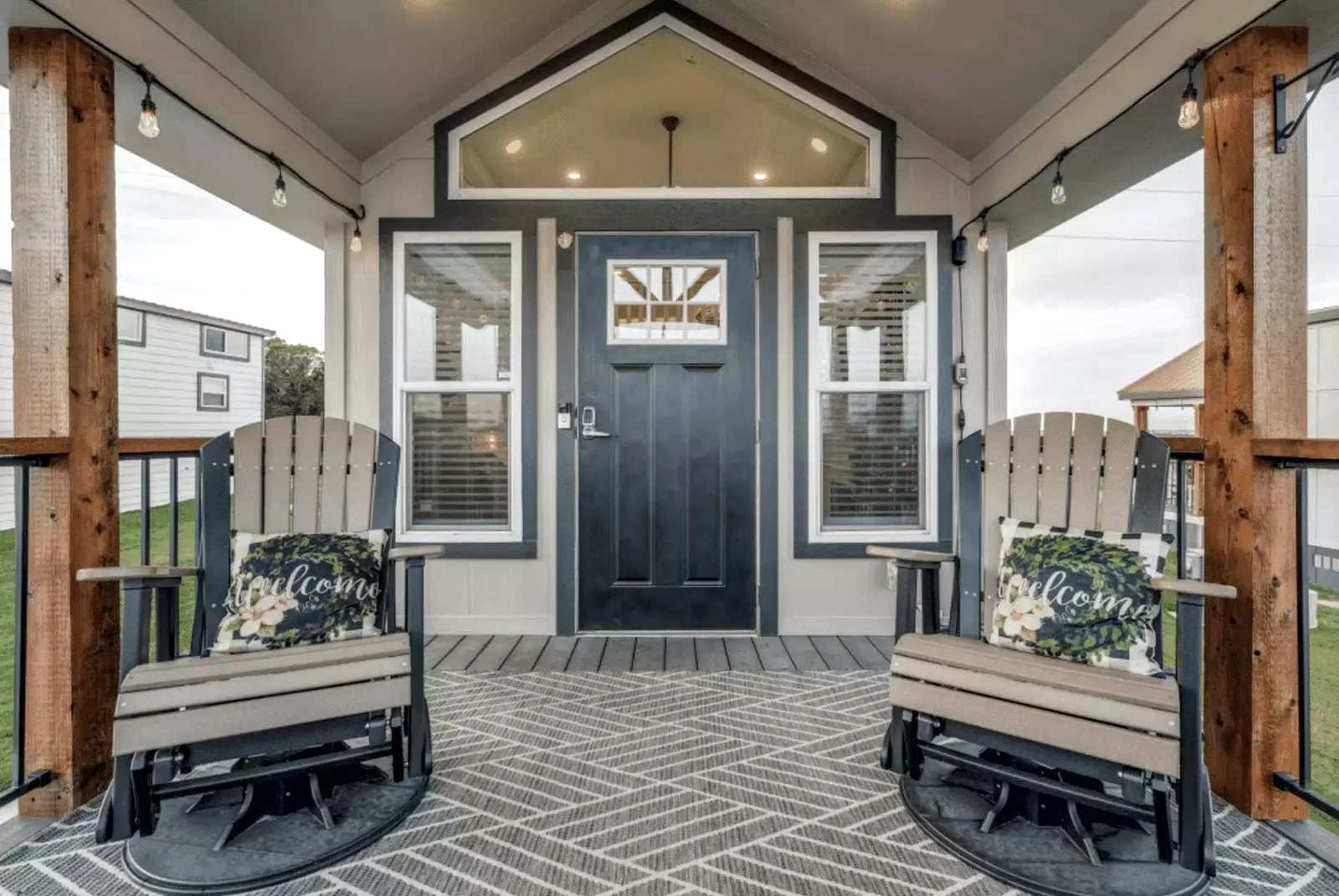 A covered porch with two Adirondack chairs, a dark front door, and a welcome sign.