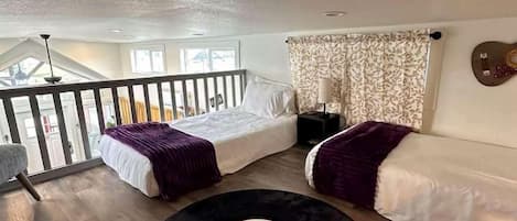 A room with a loft bed, a sofa, a record on the floor, and a guitar on the wall.