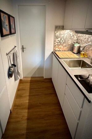 Eine kleine Küche mit Holzboden, Spüle und einer Rückwand mit sechseckigen Fliesen.