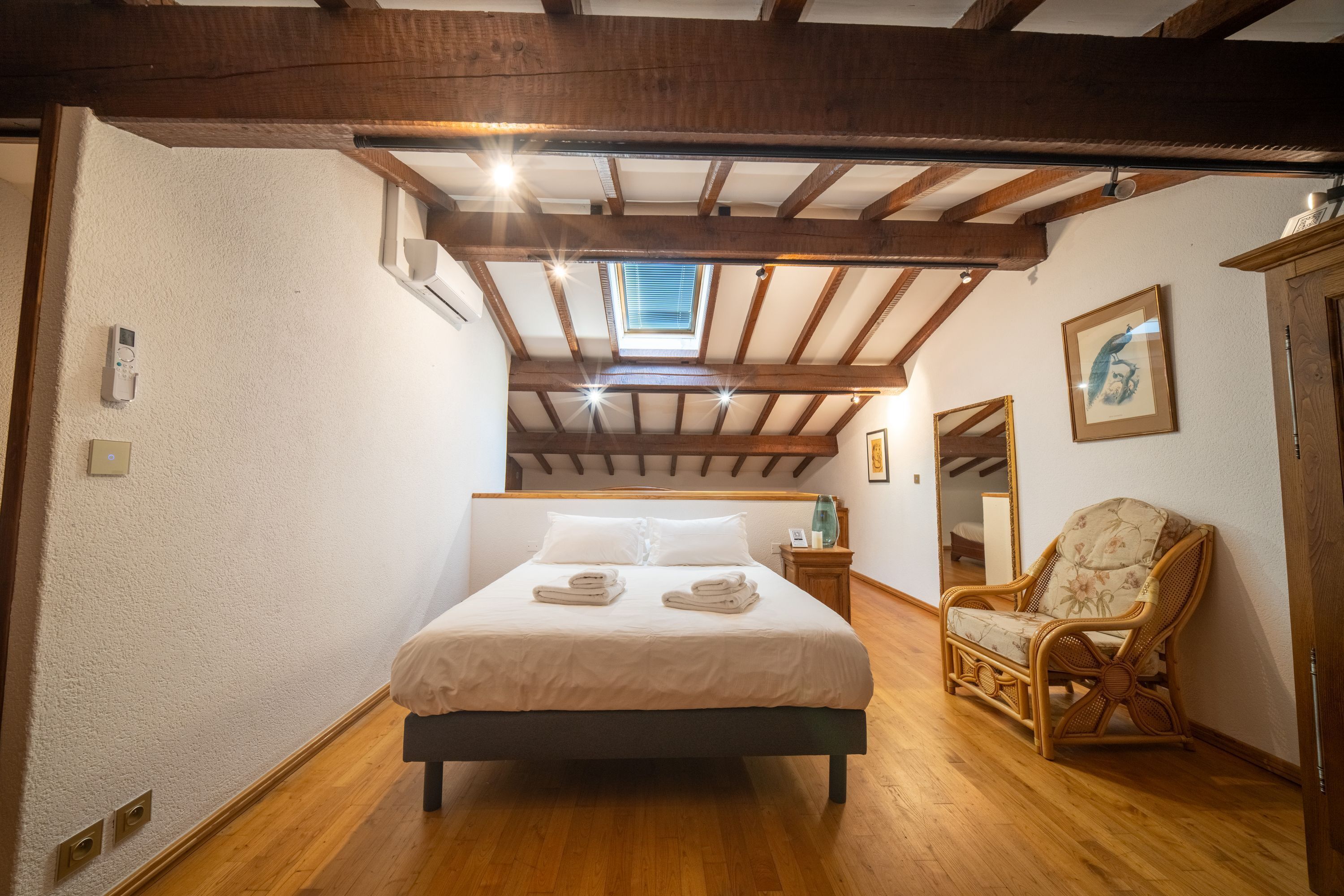A bedroom with a bed, a chair, a mirror, and a skylight.