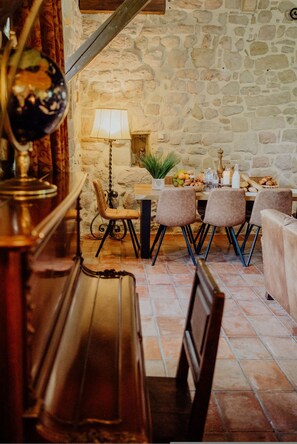 Un interior rústico con paredes de piedra, un banco de madera, una mesa con sillas, una lámpara y un globo terráqueo.