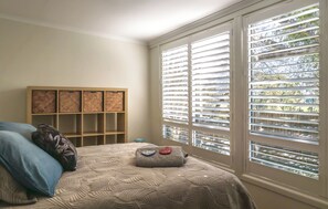 A bedroom with a bed, a wooden storage unit, and a window with blinds. - Handleys Cottage | Pet Resorts Australia Adjacent (High Range)