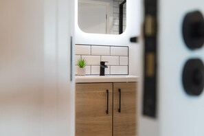 Una cocina moderna con encimera blanca, grifo negro, planta en maceta y armarios de madera.