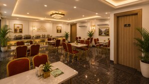 Ein Hotel-Essbereich mit Marmorböden, rot gepolsterten Stühlen, einer Chandelüster und einem Buffet.