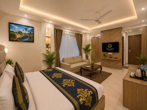 A hotel room with a bed, a sofa, a TV, a desk, and a ceiling fan. - Hotel Decent Premier -Delhi Airport (New Delhi)